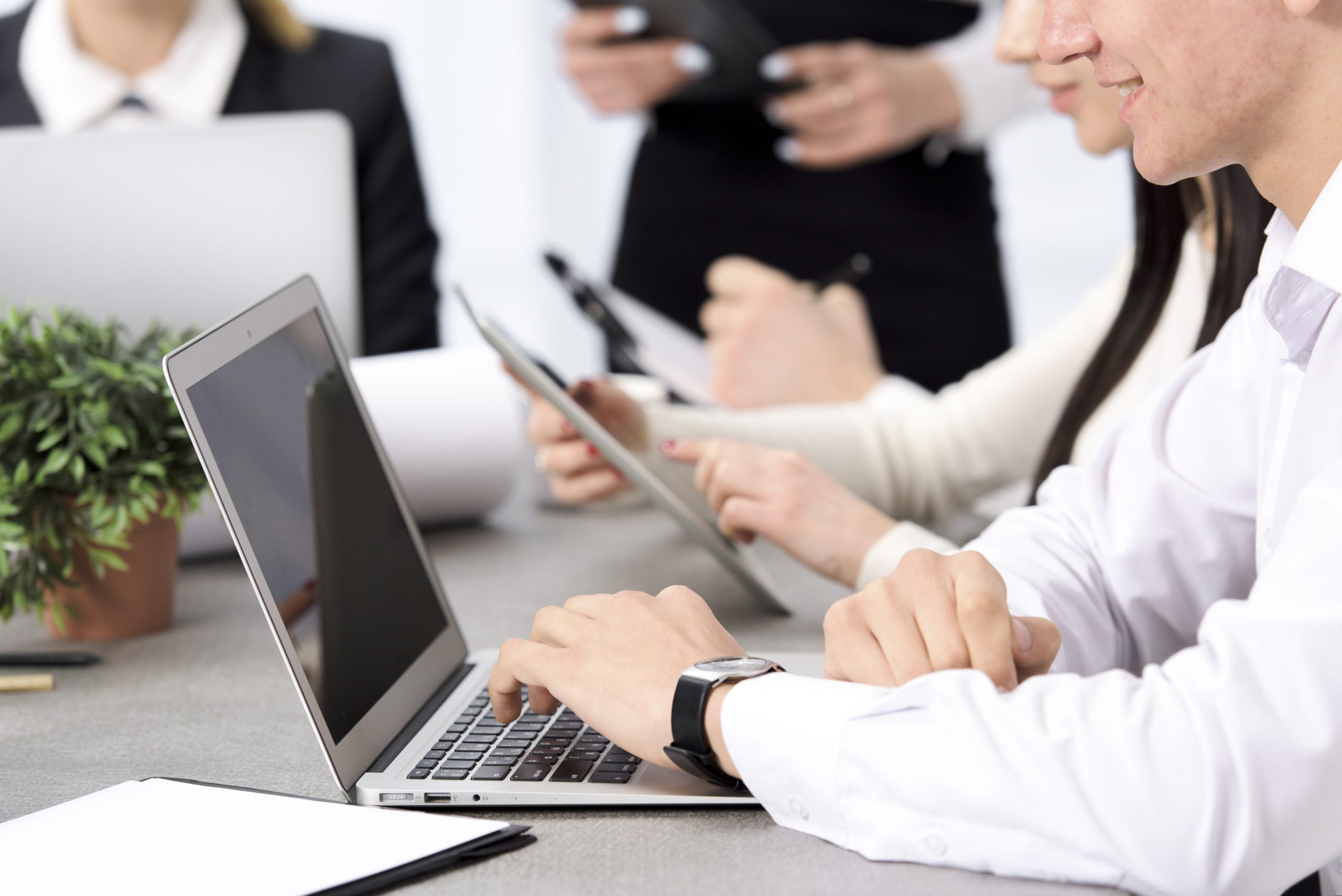 smiling-businessman-s-hand-using-laptop-sitting-with-his-colleague-desk